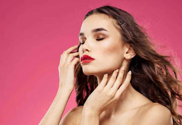 Sexy Brünette mit roten Lippen auf rosa Hintergrund berühren ihre Haare mit ihren Händen — Stockfoto