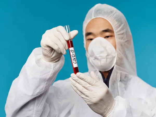 Чоловік лабораторії азіатського вигляду аналізує кров'яний тест на ковідо-19 синій фон — стокове фото