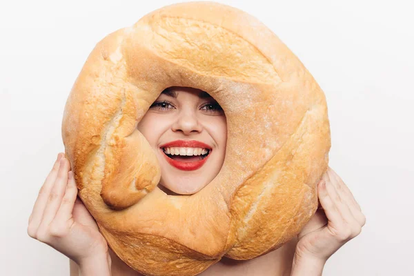 Mujer feliz con maquillaje brillante sostiene una barra redonda de pan en su mano y muecas en la cámara —  Fotos de Stock