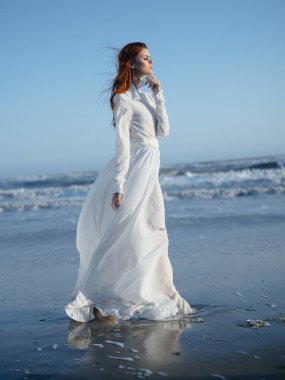 Okyanus kıyısındaki mavi gökyüzü kumsalında uzun elbiseli romantik kadın.