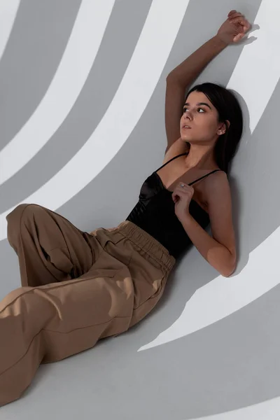 Una mujer se sienta en el suelo con ropa de moda y una sombra que cae en una habitación luminosa —  Fotos de Stock