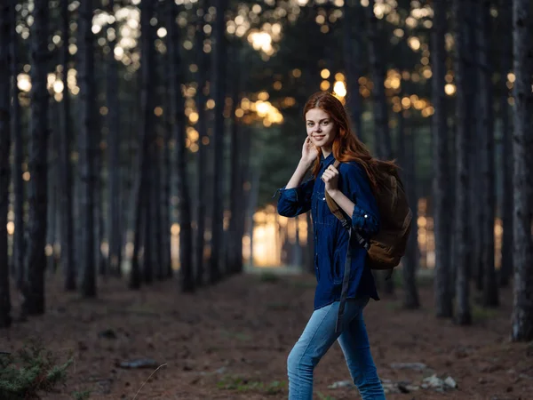Γυναίκα ταξιδεύουν Μεταξύ των δέντρων στο δάσος το φθινόπωρο και το ηλιοβασίλεμα στο παρασκήνιο — Φωτογραφία Αρχείου