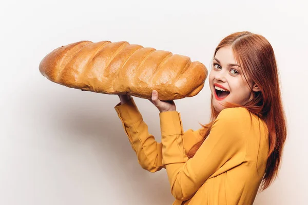 Mujer comiendo un pan grande sobre un fondo claro y un modelo de pelo rojo camisa amarilla —  Fotos de Stock