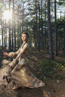 Sundress giymiş kadınlar ormanda ve günbatımı ağaçlarında ellerini doğada gezdirirler.