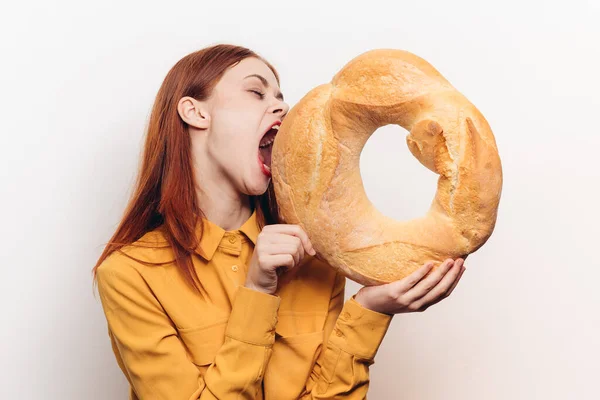 Emotional woman with a round loaf of bread and in a yellow shirt on a light background — Stock Photo, Image