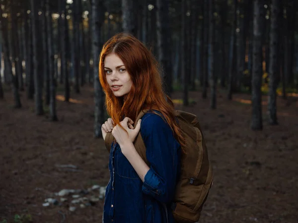 Vista lateral de una mujer con una camisa azul en un bosque de pinos con una mochila en la espalda —  Fotos de Stock