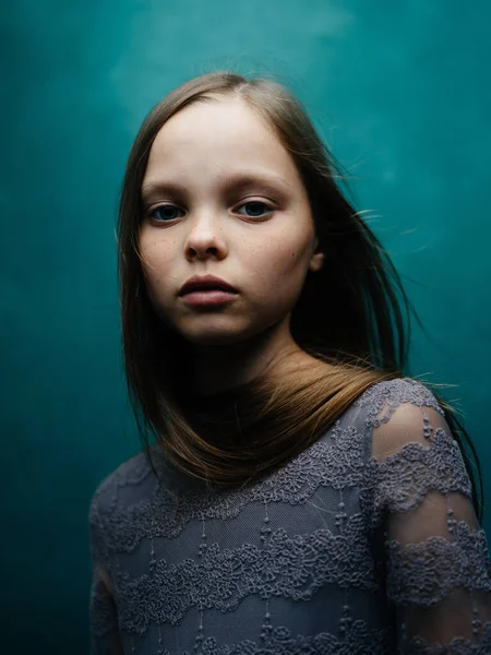 Beautiful little girl in a gray dress close-up cropped view blond hair turquoise background — Stock Photo, Image