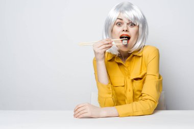 Sarı gömlekli güzel kadın beyaz peruklu suşi yiyor.