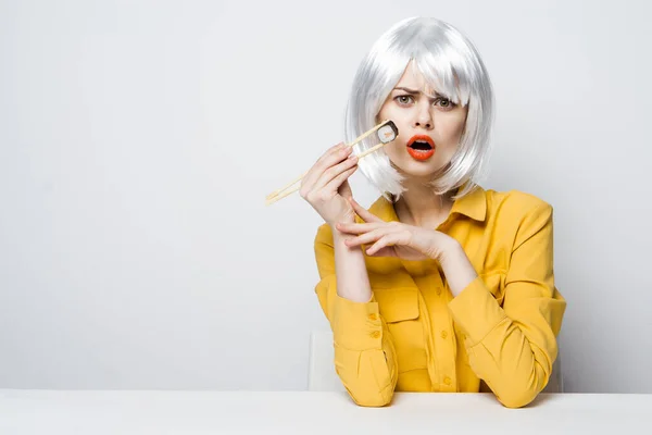 Bonita mujer en camisa amarilla peluca blanca rollos de sushi comer — Foto de Stock