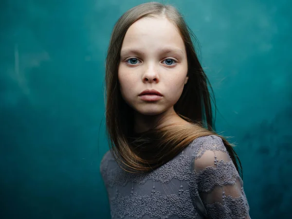 Portrait d'une belle petite fille en robe grise sur fond turquoise et yeux bleus — Photo