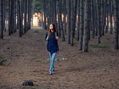 Sırtında sırt çantası ve mavi gömleğiyle ormanda dolaşan güzel bir kadın.