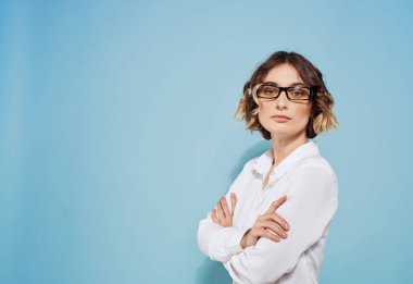 Mavi arka plan ve gözlüklü beyaz gömlekli, kısa saçlı güzel bayan.