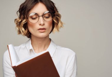 Elinde not defteri ve gri arka planda beyaz gömleği olan akıllı bir kadın.