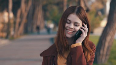 Güzel bir kadın telefonda konuşuyor. Dışarıda yürüyüş yapıyor.