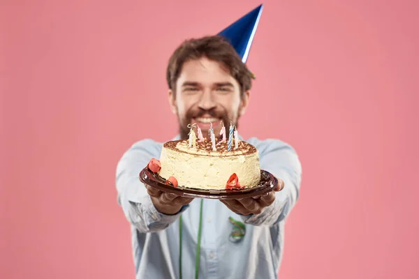 Man with cake in a plate and in a blue shirt on a pink background birthday holidays cropped view