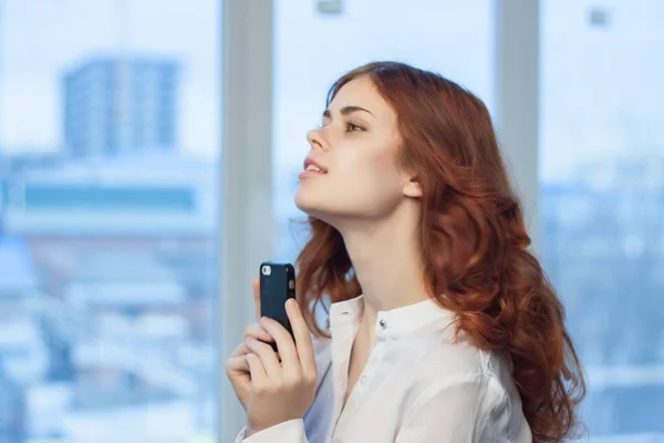 Рыжая женщина с телефоном в руках в офисной техники — стоковое фото