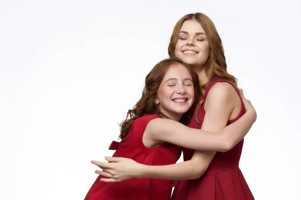 Mãe alegre e filha ao lado de vestidos vermelhos abraços estilo de vida luz fundo sorriso — Fotografia de Stock