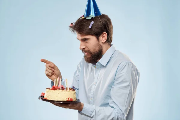 Hombre con un plato de pastel y una vela festiva fondo azul gorra fiesta corporativa — Foto de Stock