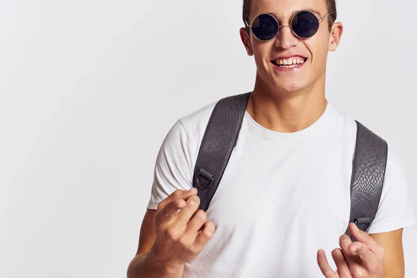 Красивый мужчина с рюкзаком на спине жестикулирует руками в футболке и в очках — стоковое фото