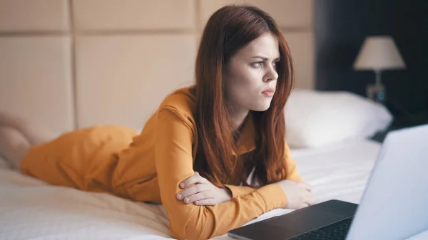 Woman lies in bed in front of laptop emotions technology freelance — Stock Photo, Image