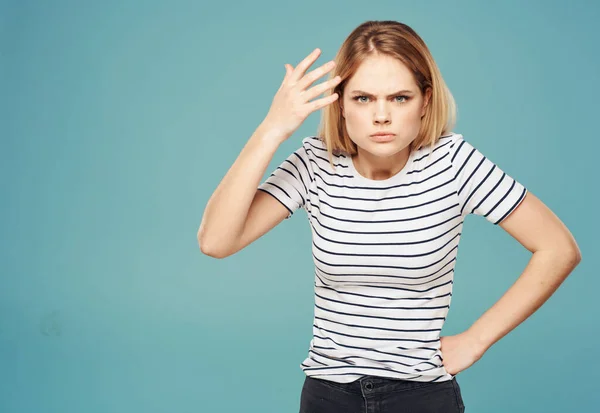Нервная женщина в полосатой футболке жестикулирует руками на синем фоне — стоковое фото