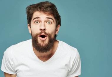 Mavi arka planda beyaz tişörtlü ve kalın bıyıklı duygusal bir adamın portresi.