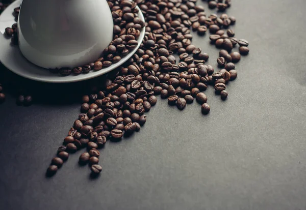 Taza blanca y platillo y granos de café grandes sobre un fondo oscuro macro fotografía — Foto de Stock