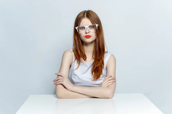 Κομψή γυναίκα με γυαλιά κάθεται στο τραπέζι κόκκινα χείλη στούντιο lifestyle — Φωτογραφία Αρχείου