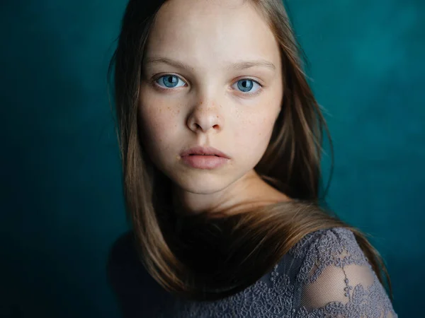 Retrato de una hermosa niña con un vestido gris sobre un fondo turquesa y ojos azules — Foto de Stock