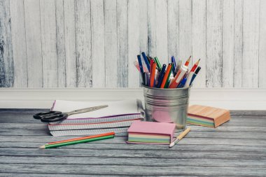 Demir bir bardakta kırtasiye malzemeleri ve bir paket çıkartma kalemleri not defteri.