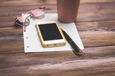 cep telefonu kahve fincanı beyaz kağıt bardaklar ve masada bir kalem.