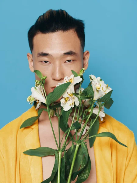 Homem coreano bonito em um casaco amarelo com um buquê de flores brancas em um modelo de fundo azul — Fotografia de Stock