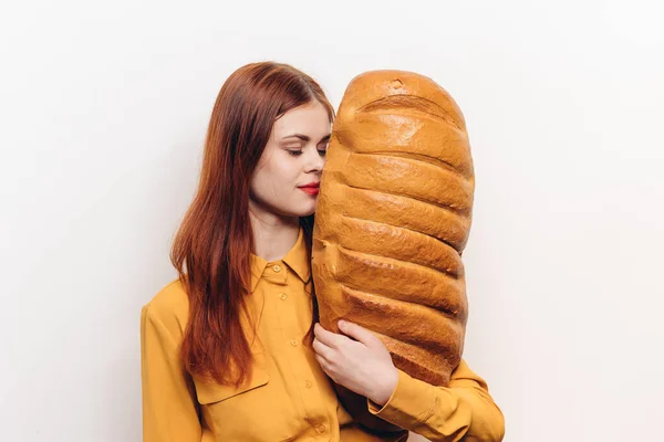 Grande pagnotta di pane in mano a una donna in camicia gialla su sfondo chiaro — Foto Stock