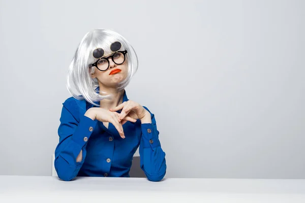 Fröhliche Frau mit weißer Perücke, roten Lippen, dunkler Brille sitzt im blauen Hemd an einem Tisch — Stockfoto