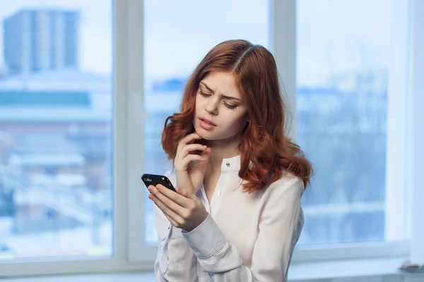 Fröhliche rothaarige Frau mit einem Telefon in der Hand, das ein offizielles Büro kommuniziert — Stockfoto