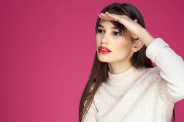 Uzun saçlı, kırmızı dudaklı beyaz bluzlu, pembe arka planlı çekici bir kadın.