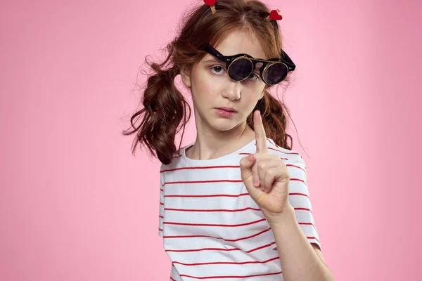 Petite fille dans des lunettes et des pinces à linge à la mode sur ses cheveux émotions fond rose coeurs — Photo