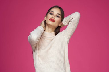 Kırmızı dudaklı, makyajlı beyaz bluzlu, uzun saçlı, pembe arka planlı bir kadın.