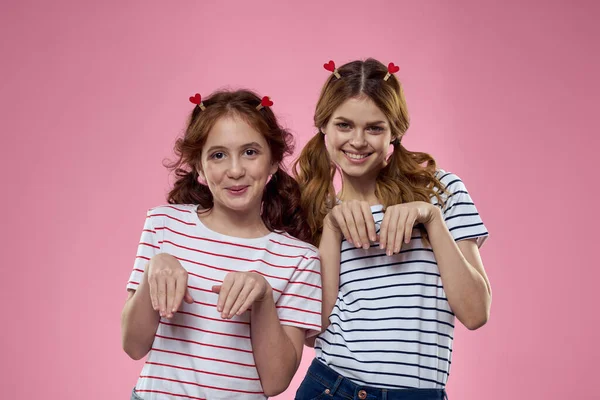 Ευτυχισμένες αδελφές διασκεδάζουν σε ένα ροζ φόντο και σε σχήμα καρδιάς μανταλάκια στα κεφάλια τους — Φωτογραφία Αρχείου
