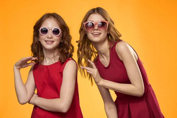 Cheerful mom and daughter wearing sunglasses lifestyle friendship family yellow background studio — Stock Photo, Image