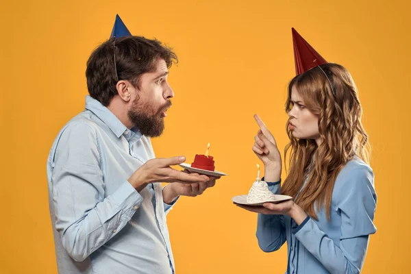 Festa di compleanno uomo e donna in un cappello con una torta su uno sfondo giallo vista ritagliata — Foto Stock