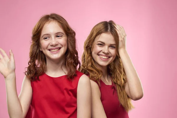 Mamá e hija en vestidos rojos abrazos divertido mueca infancia alegría rosa fondo —  Fotos de Stock