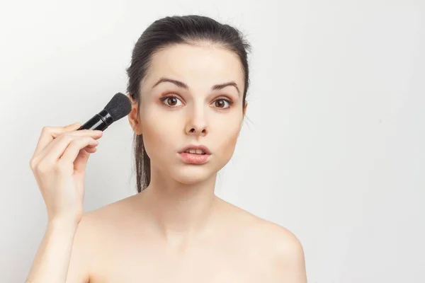 Mulher com ombros nus com uma escova nas mãos aplicando maquiagem — Fotografia de Stock