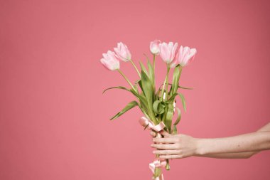 Pembe arka planda bir kadının ellerinde bir buket çiçek.