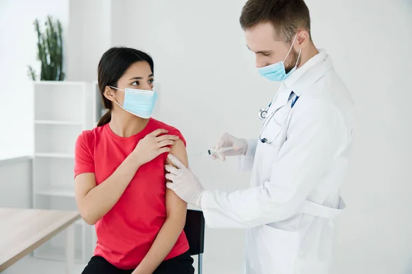 Man läkare i en medicinsk mask injicera en kvinnlig patient i axeln covid vaccination — Stockfoto