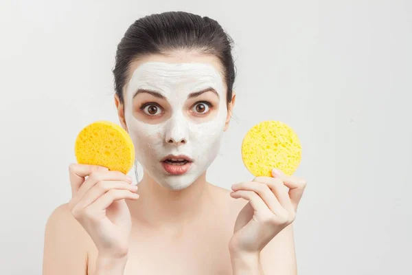 emotional woman with bare shoulders wipes a mask on her face with sponges