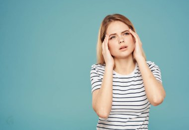 Kafası karışmış bir kadın, mavi bir arka plan modeli üzerinde elleriyle yüzüne dokunuyor. Stres duyguları.