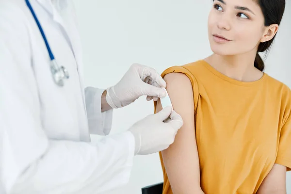 A doctor in protective gloves to stick an injection plaster on a woman vaccination — Stockfoto