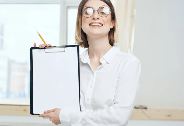 Žena drží složku s bílým papírem a oknem v pozadí. — Stock fotografie