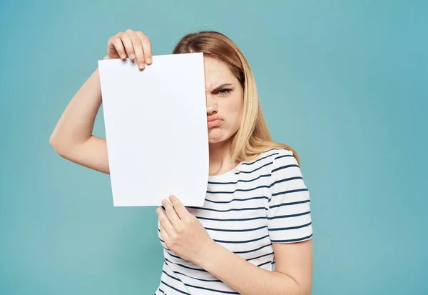 Femme blonde émotionnelle avec une feuille blanche de papier dans ses mains sur un fond bleu — Photo